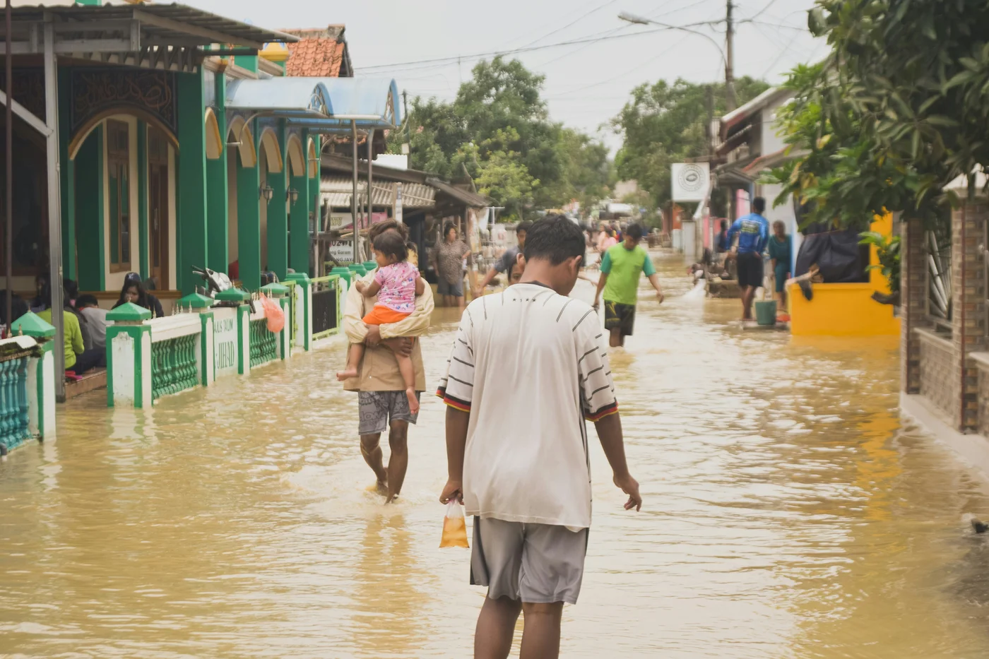 People wading through floodwater along a residential street
