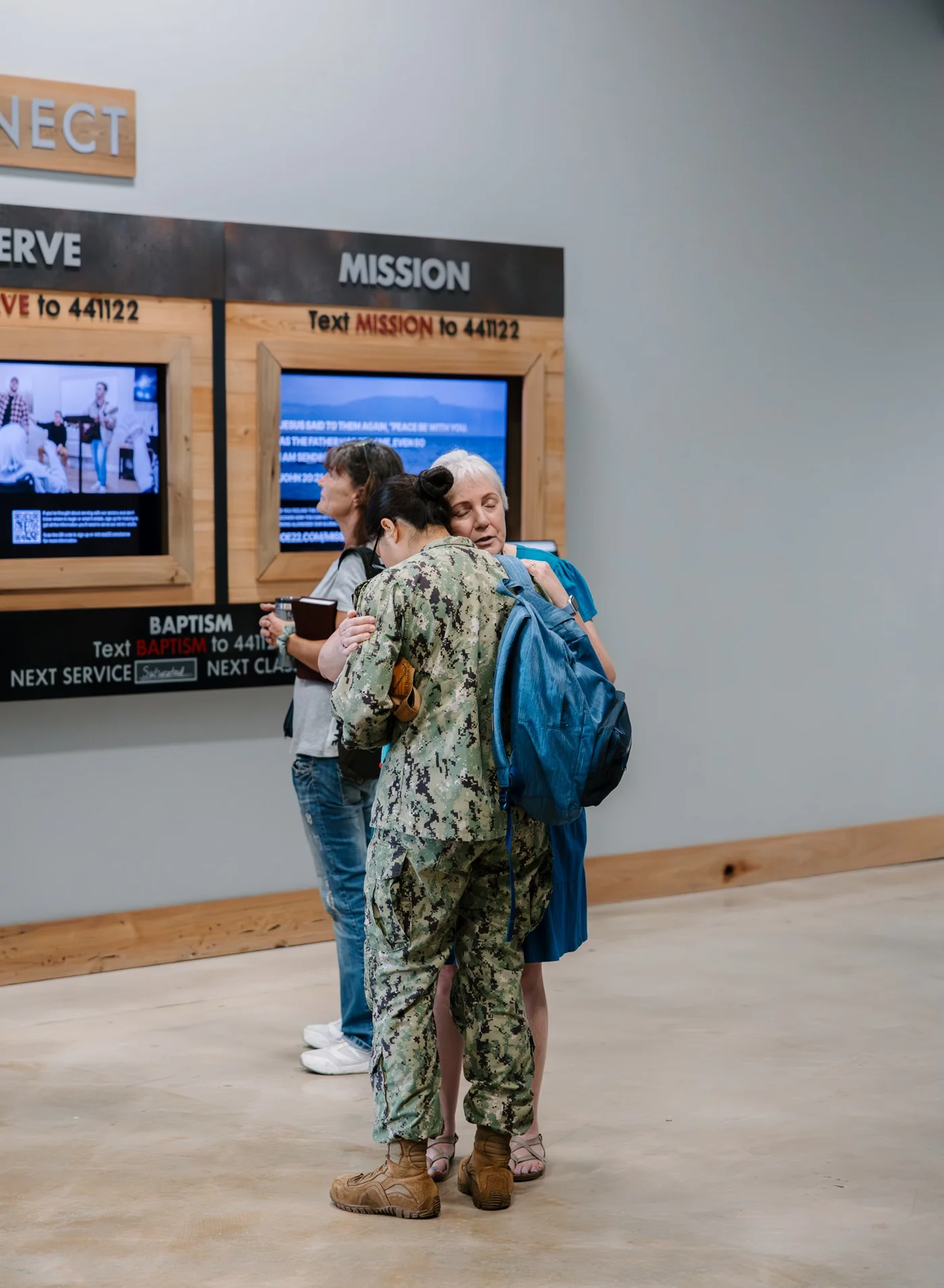 A person in military uniform embracing a woman in a church lobby