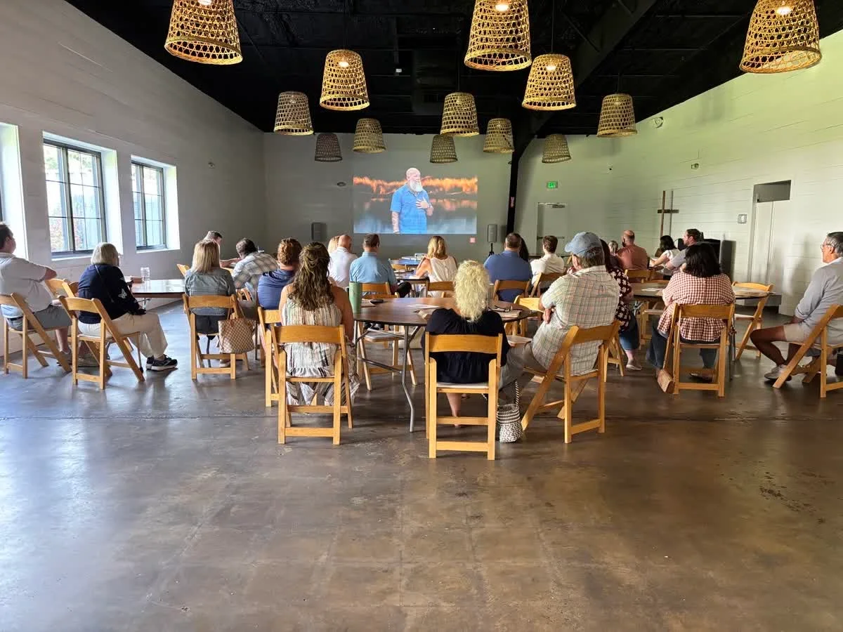 People gathered at tables watching a sermon projected onto a wall